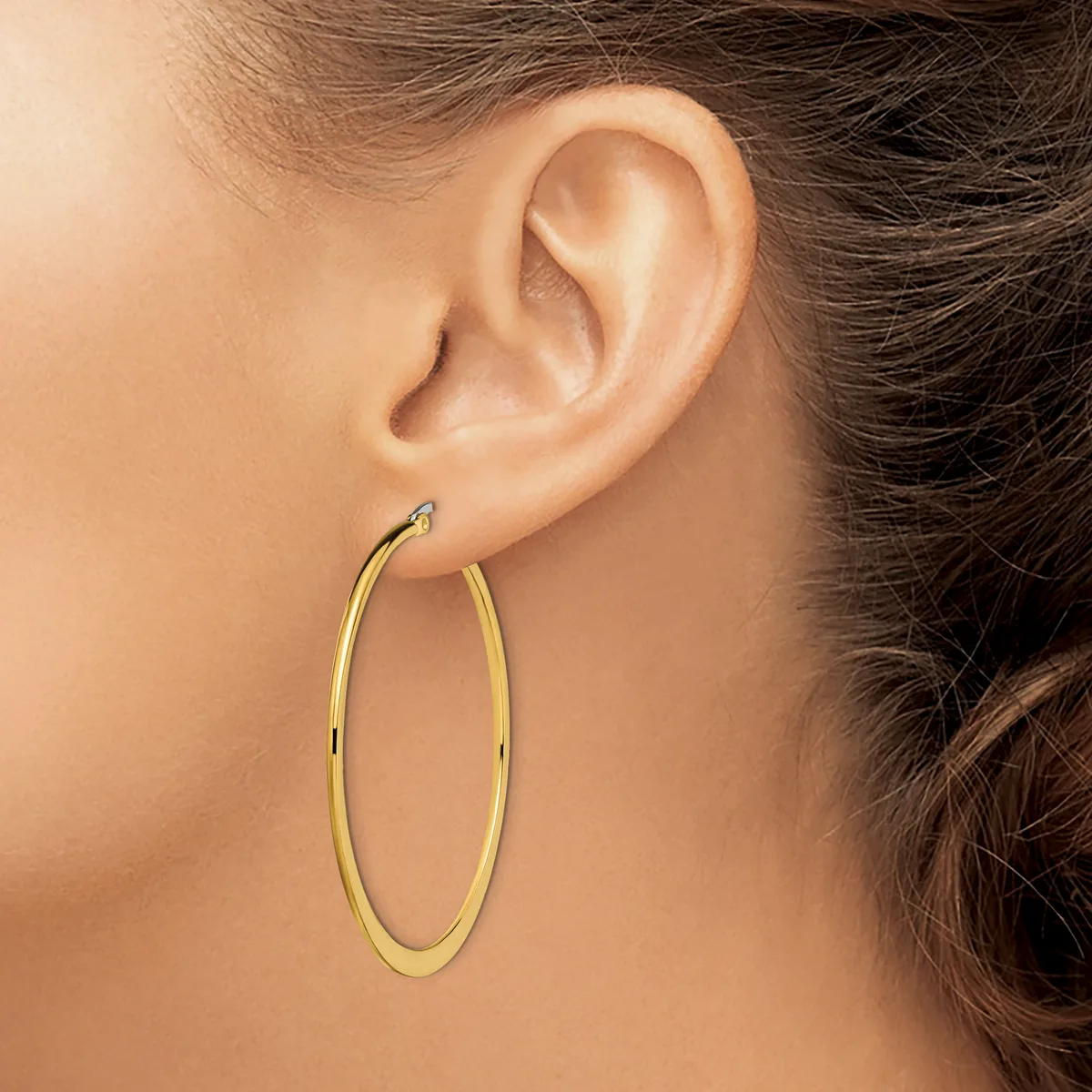 A woman wearing large oval gold hoop earrings, shown in profile from the side of her face and ear.