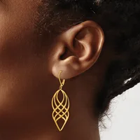 A gold-toned elongated leaf-shaped earring with interlocking geometric cutouts hangs from a wire hook on a model's ear.
