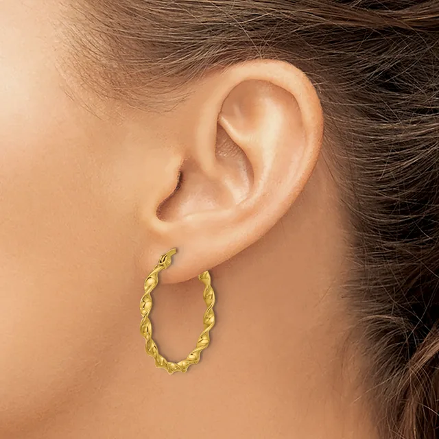 A woman wearing a twisted gold hoop earring in her earlobe, shown from the side view of her ear and neck.