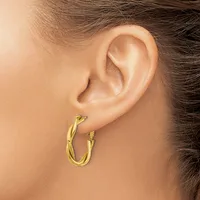 A person wearing a pair of twisted gold hoop earrings, shown from the side profile of their ear and neck.