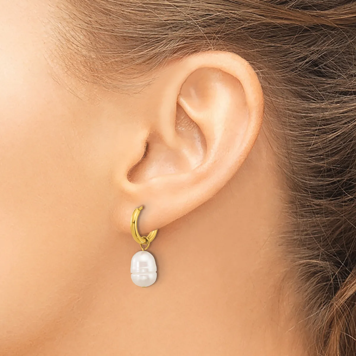 A person wearing a gold-toned hoop earring with a white pearl pendant hanging from the lobe.