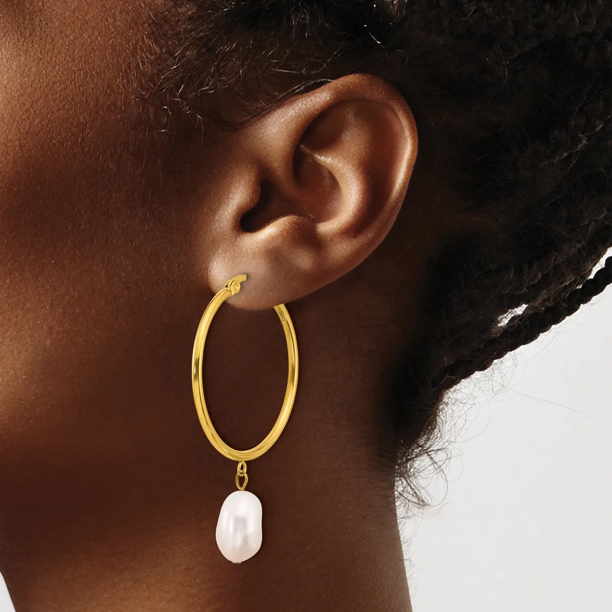 A person wearing a gold hoop earring with a white pearl pendant hanging from the bottom.