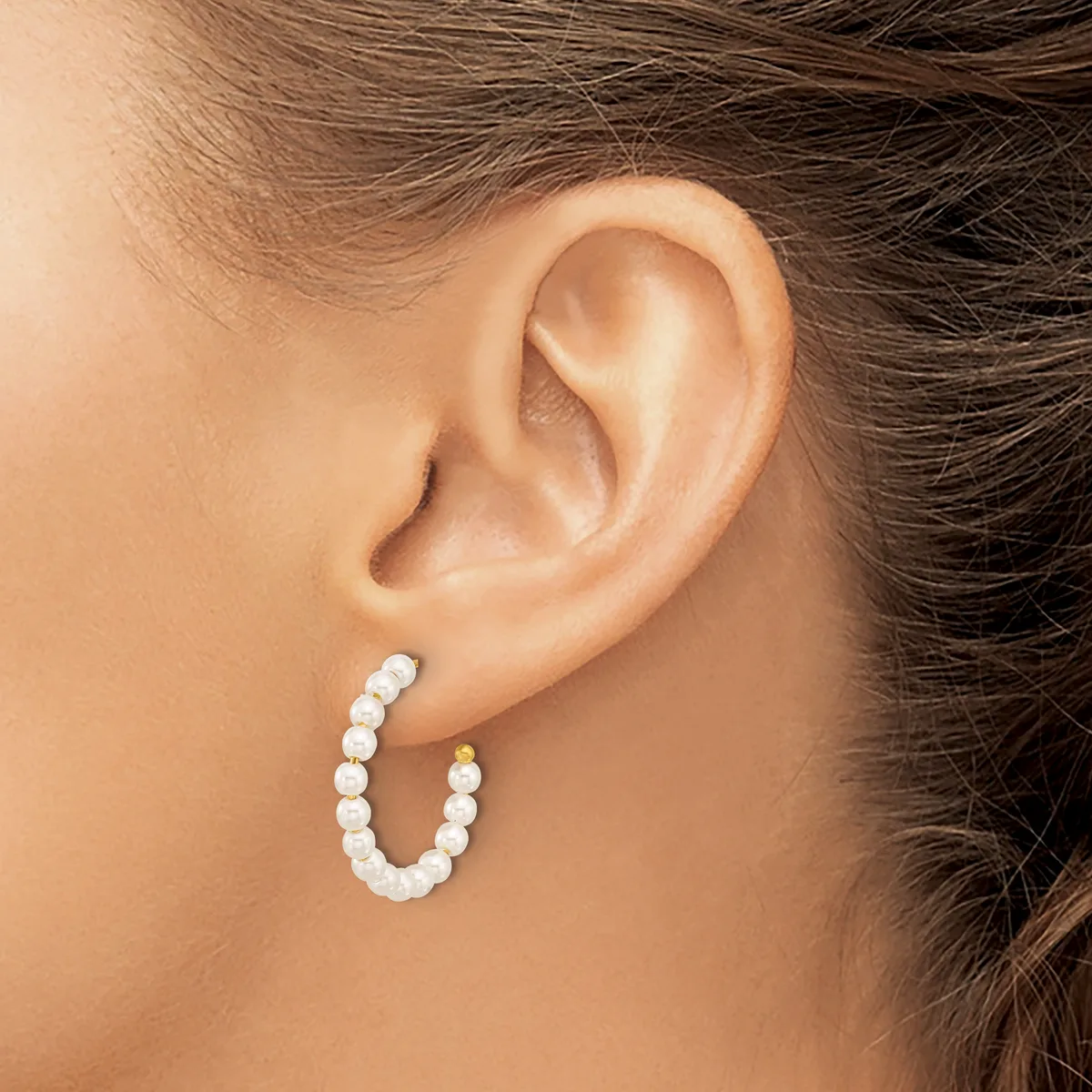 A person wearing a curved pearl hoop earring in their earlobe, shown from the side view of their ear and neck.