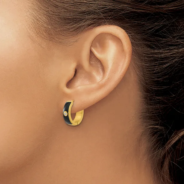 A person wearing a small gold and black enamel hoop earring with a small stamped hallmark, shown from the side view of their ear and neck.
