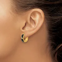 A person wearing a small gold and black enamel hoop earring with a small stamped hallmark, shown from the side view of their ear and neck.