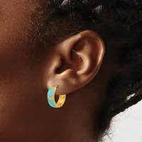A person wearing a gold and turquoise enamel hoop earring with small red stone accents, shown from the side view against their ear.