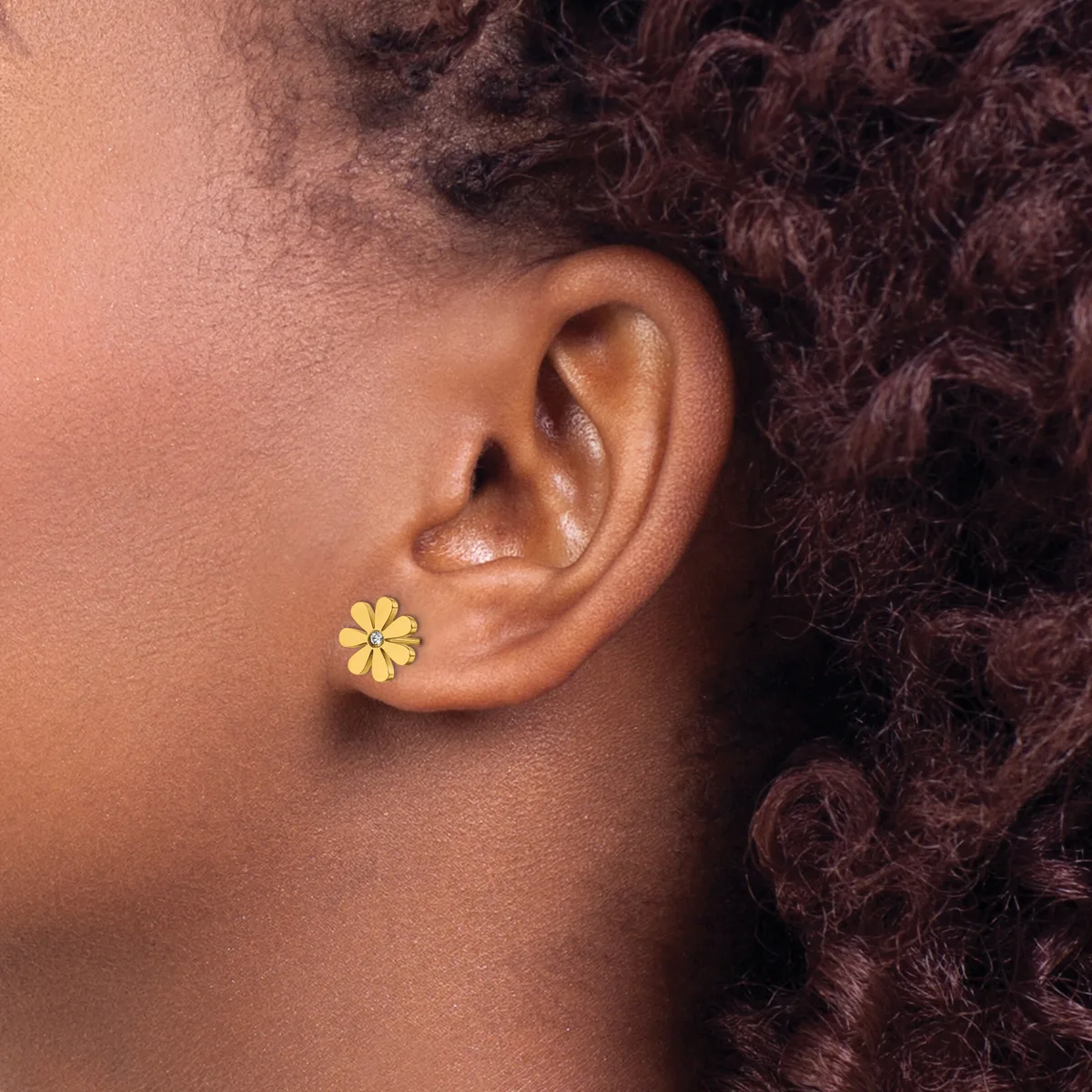 A person wearing a small yellow flower-shaped stud earring in their earlobe, shown in profile against their neck and dark curly hair.