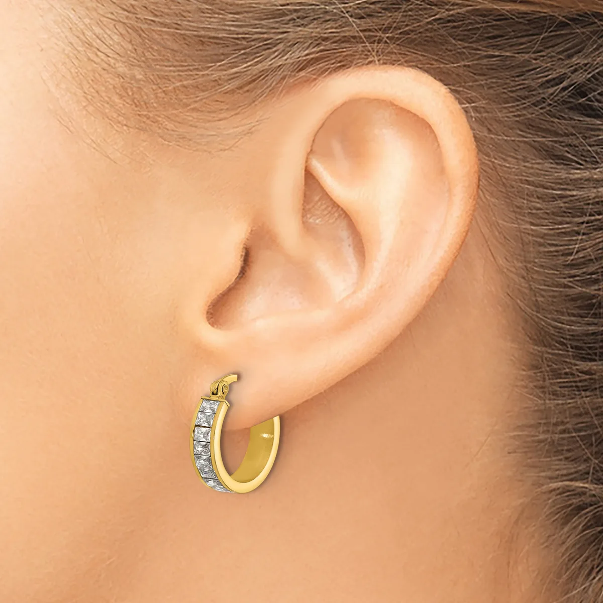A woman wearing a two-tone hoop earring with a gold outer surface and diamond or crystal embellishments along the upper curved edge.