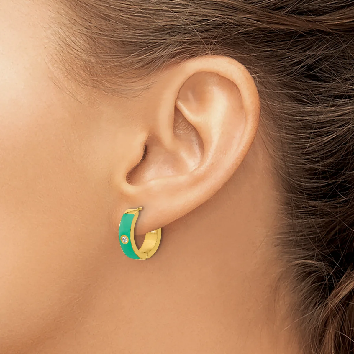 A person wearing small hoop earrings with green and gold coloring and a small rhinestone detail, shown from the side view of their ear.