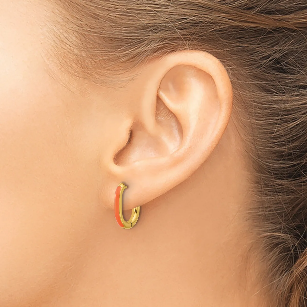 A small hoop earring with red and gold coloring in a person's earlobe, shown from the side view of their ear and neck.
