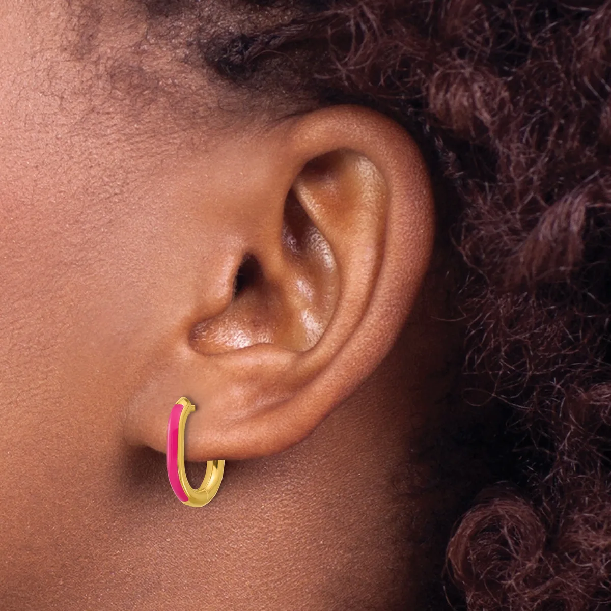 A person wearing a pink and gold hoop earring in their earlobe, shown in profile view.