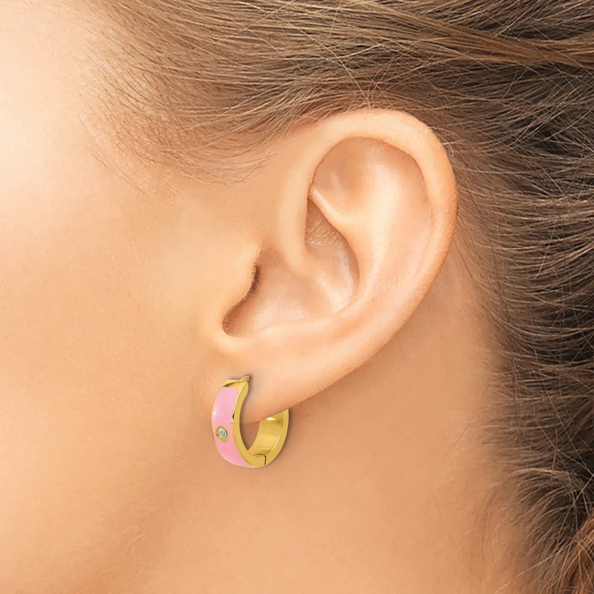 A person wearing small gold and pink enamel hoop earrings, shown from the side view of their ear and neck.
