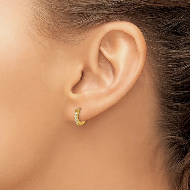 A small gold hoop earring with diamond accents worn on the earlobe of a person shown in profile.