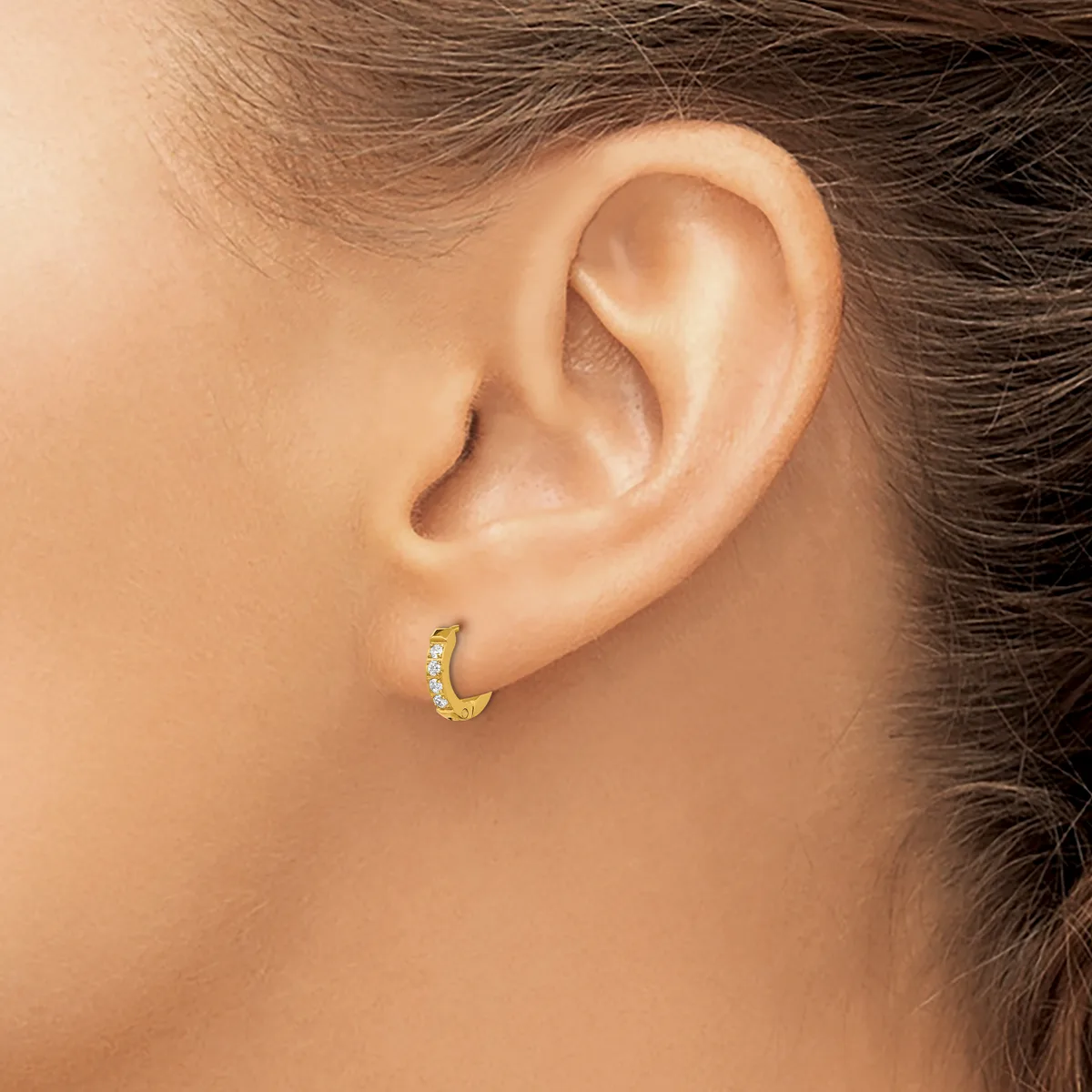 A small gold hoop earring with diamond accents worn on the earlobe of a person shown in profile.