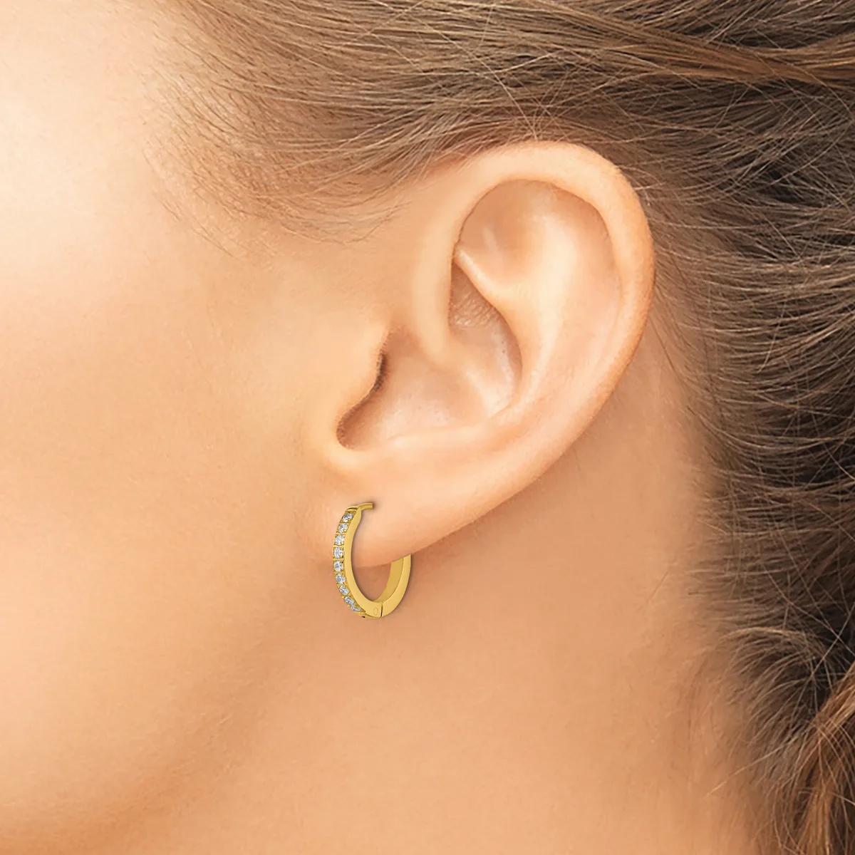 A woman wearing a gold hoop earring with diamond accents on her earlobe, shown from the side profile.