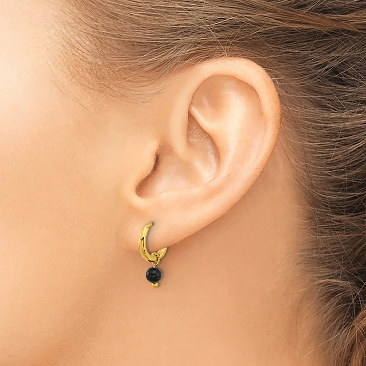 A person wearing a gold-toned hoop earring with a small black spherical bead pendant hanging from it.