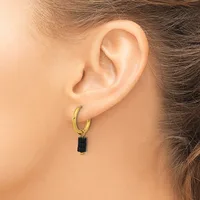 A gold-toned hoop earring with a small black rectangular pendant hangs from a person's earlobe.