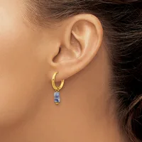 A gold hoop earring with a small rectangular blue stone pendant hangs from a woman's earlobe.