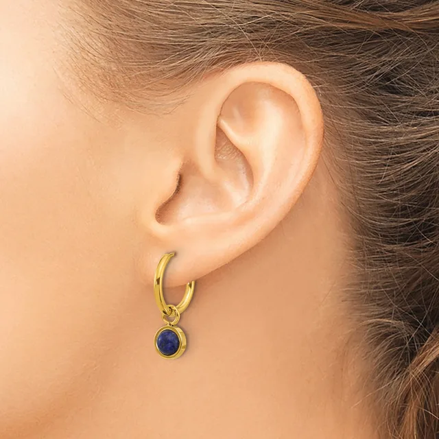 A person wearing a gold hoop earring with a small round blue stone pendant hanging from it.
