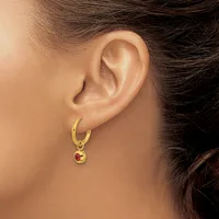 A person wearing a gold hoop earring with a small circular pendant featuring a red stone hangs from their earlobe.