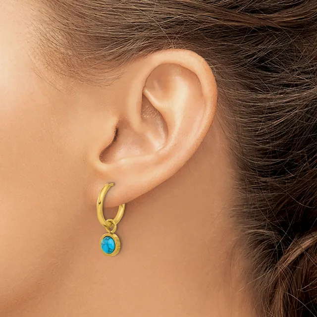 A person wearing a gold hoop earring with a small turquoise oval stone pendant hanging from it.