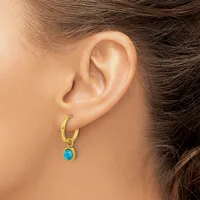 A person wearing a gold hoop earring with a small turquoise oval stone pendant hanging from it.