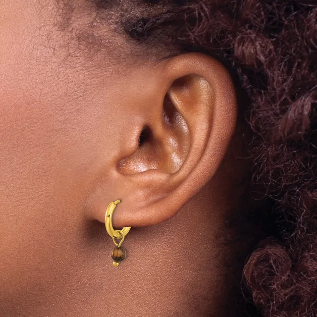 A person wearing a gold-toned hoop earring with a small brown spherical bead attached to the bottom, shown from the side profile of their ear.