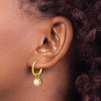 A close-up side view of a person's ear wearing a gold hoop earring with a white pearl pendant hanging from it.
