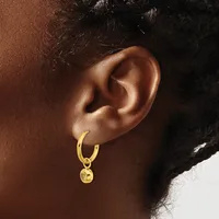 A gold hoop earring with a small dangling charm hangs from the earlobe of a person shown in profile.