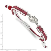 A burgundy and white braided bracelet with a silver rectangular charm connector and beaded ends, shown against a measurement scale.