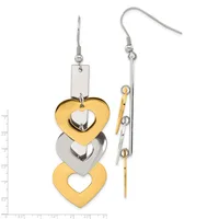 Pair of mismatched dangling heart earrings in gold and silver tones with fish hook closures, shown against a measurement scale.