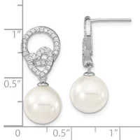 A pair of silver drop earrings with cubic zirconia-paved tops featuring heart-shaped designs and white pearl pendants, displayed on a measurement scale.