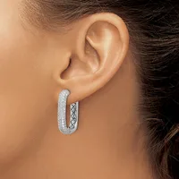 A woman wearing a U-shaped hoop earring with a textured outer surface and decorative filigree pattern visible on the inner side.