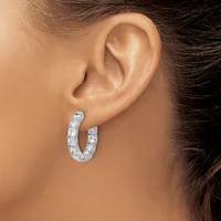 A person wearing a pair of silver hoop earrings with a textured, hammered finish, shown from the side profile view.