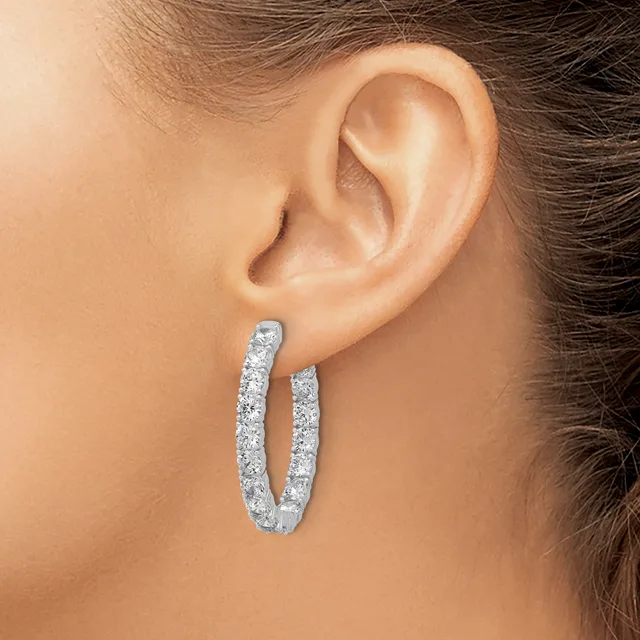 A woman wearing a U-shaped hoop earring with diamond-like stones set throughout the curved surface, shown from the side against her ear.