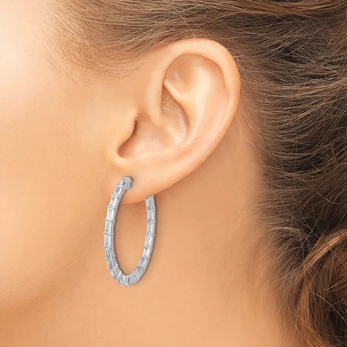 A woman wearing a textured silver hoop earring visible from the side profile, with her ear and part of her hair shown against a neutral background.