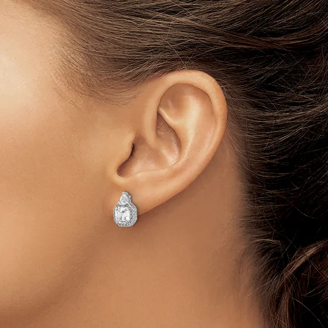 A person wearing a teardrop-shaped diamond stud earring with a halo setting in white metal, shown on their earlobe from a side profile view.