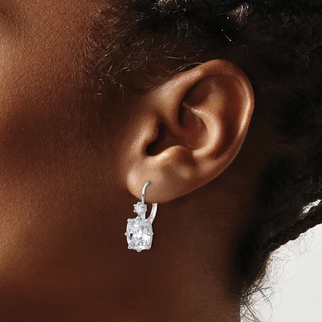 A close-up of a person's ear wearing a silver hoop earring with a cushion-cut diamond pendant hanging from it.