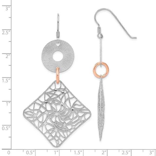 Two silver dangle earrings with fish hook backs, one featuring a circular disc with a textured diamond-shaped filigree pendant, the other a long tapered spike with a small copper ring, displayed against a ruler showing measurements up to three inches.