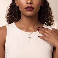 A woman wearing a white sleeveless top and silver cross pendant necklace, with curled dark hair, burgundy lipstick, and burgundy nail polish.