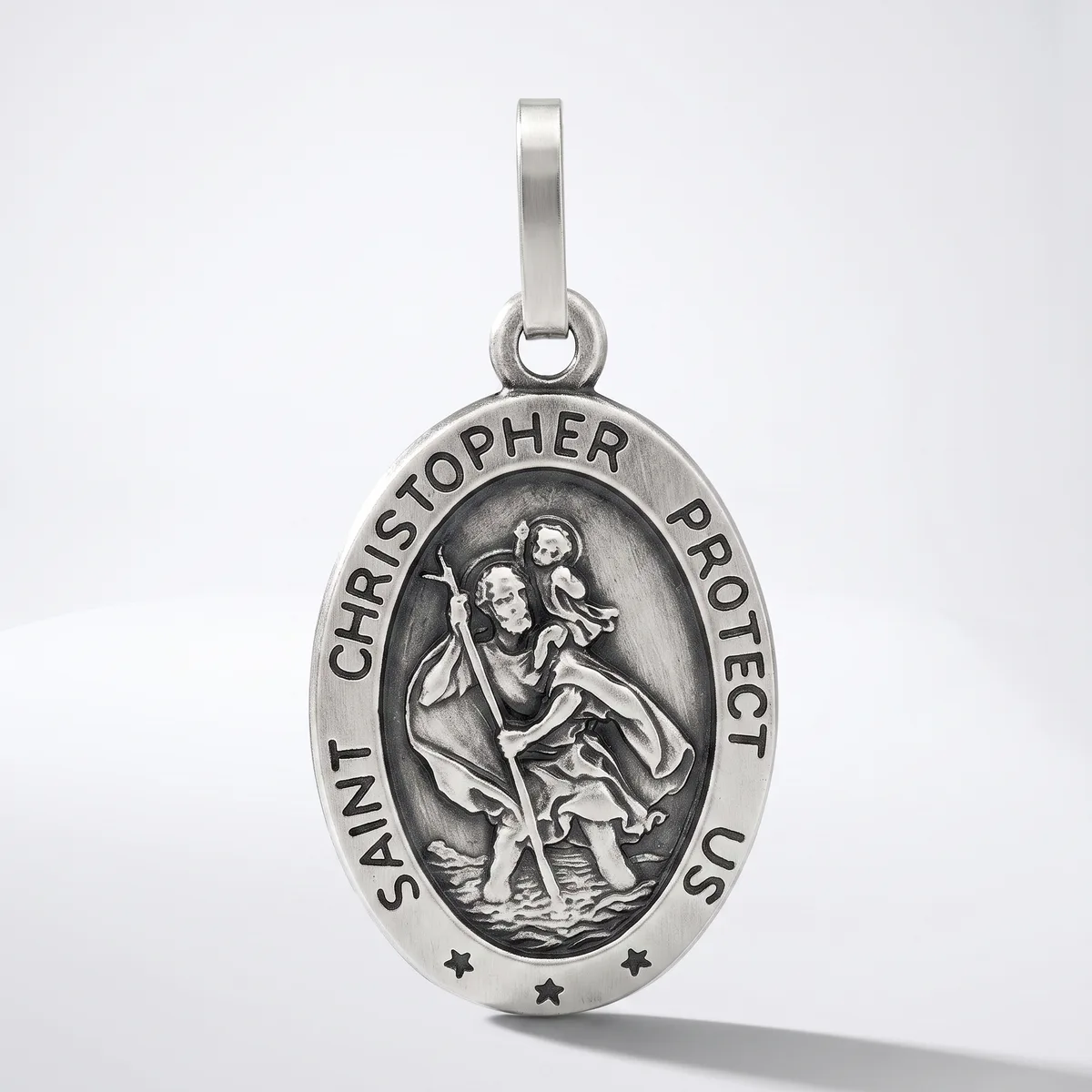 A silver oval pendant featuring Saint Christopher carrying a child, with text around the border and small stars at the bottom, suspended from a silver bail.