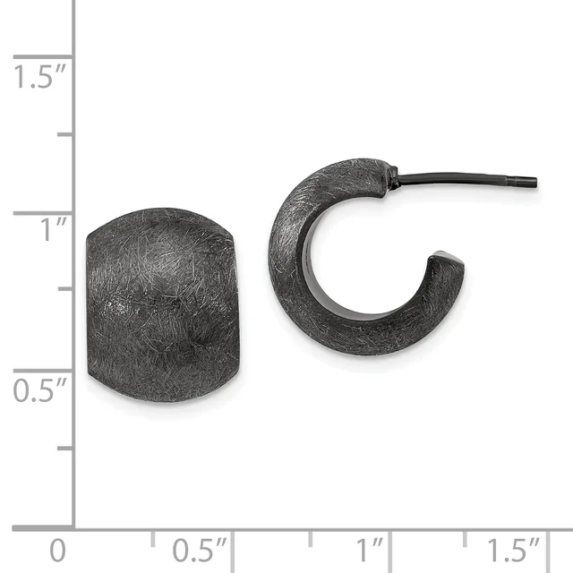 Two dark textured metal earrings displayed next to a ruler showing approximately one inch in height: a cylindrical stud on the left and a curved hoop with a post on the right.