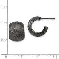 Two dark textured metal earrings displayed next to a ruler showing approximately one inch in height: a cylindrical stud on the left and a curved hoop with a post on the right.