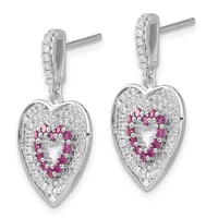 Pair of silver heart-shaped dangle earrings with diamond-paved tops, ruby gemstones arranged in a heart outline within each heart pendant, and post backs.