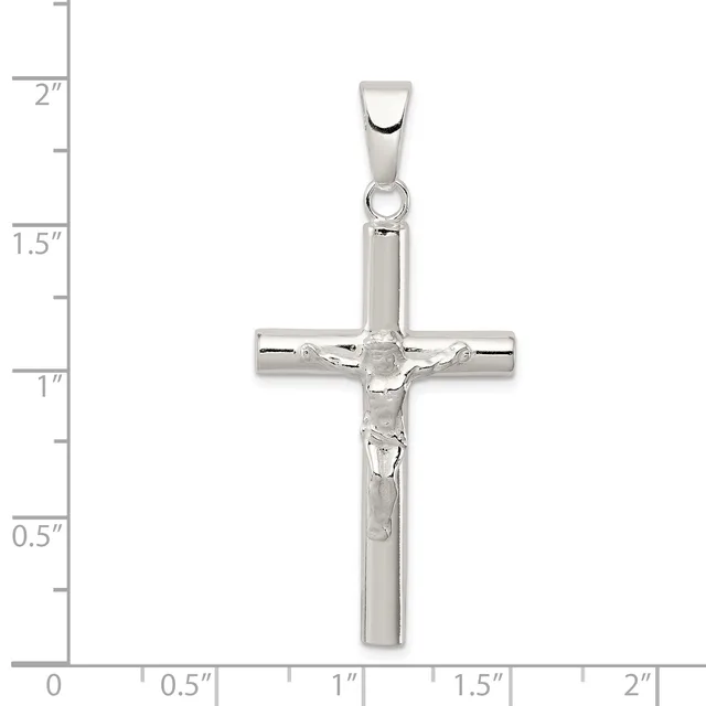 A polished silver crucifix pendant with a corpus figure, shown against a ruler measuring approximately 2 inches in height.