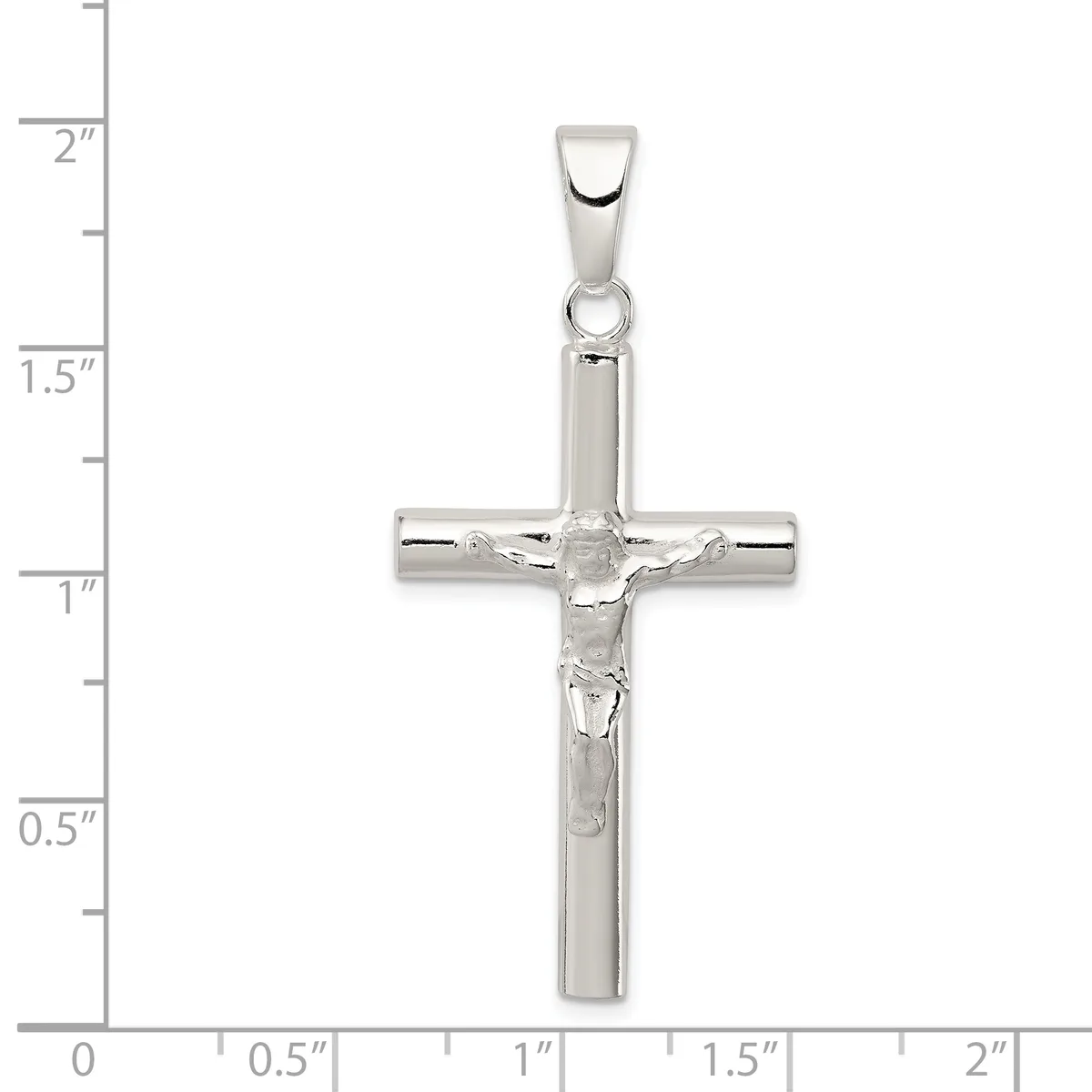 A polished silver crucifix pendant with a corpus figure, shown against a ruler measuring approximately 2 inches in height.