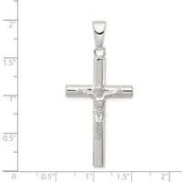 A polished silver crucifix pendant with a corpus figure, shown against a ruler measuring approximately 2 inches in height.