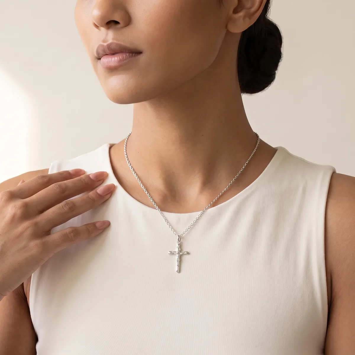A woman wearing a cream sleeveless top and a silver chain necklace with a small cross pendant.