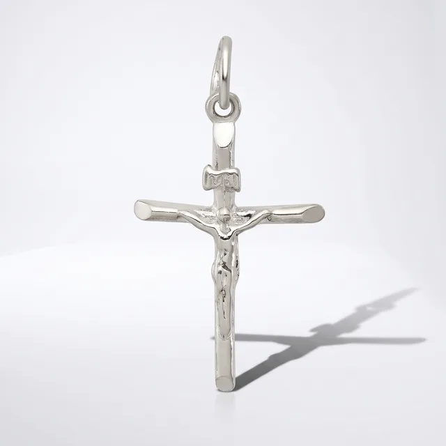 A silver crucifix pendant with a figure of Christ displayed against a white background, casting a shadow to the right.