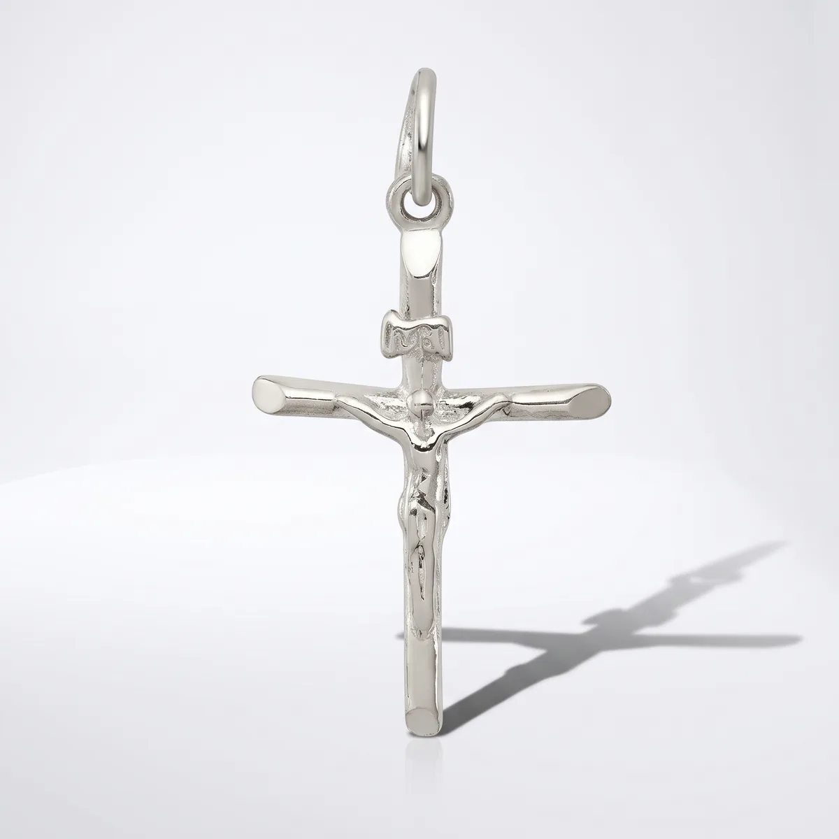 A silver crucifix pendant with a figure of Christ displayed against a white background, casting a shadow to the right.